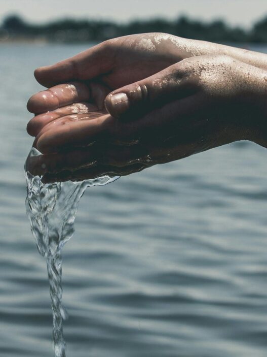 Hands collecting clean water from a river, highlighting the importance of water quality in managing autoimmune health and reducing inflammation.