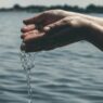 Hands collecting clean water from a river, highlighting the importance of water quality in managing autoimmune health and reducing inflammation.