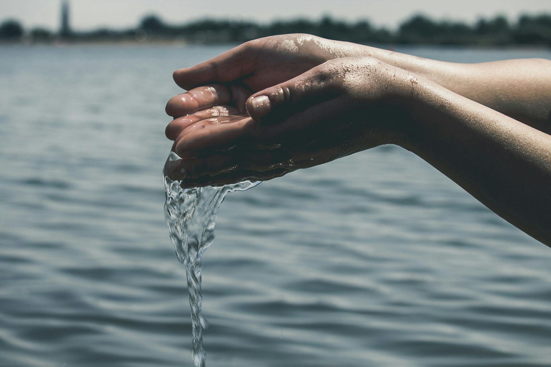 Hands collecting clean water from a river, highlighting the importance of water quality in managing autoimmune health and reducing inflammation.