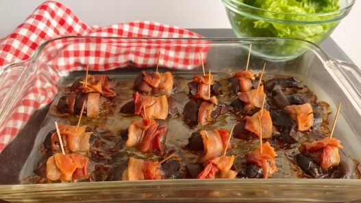 Bacon-wrapped chicken liver bites served with nutrient-dense kale, carrot ribbons, and purple cabbage salad on a wooden surface, AIP-friendly.