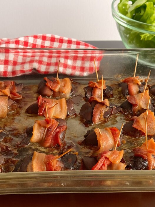 Bacon-wrapped chicken liver bites served with nutrient-dense kale, carrot ribbons, and purple cabbage salad on a wooden surface, AIP-friendly.