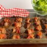 Bacon-wrapped chicken liver bites served with nutrient-dense kale, carrot ribbons, and purple cabbage salad on a wooden surface, AIP-friendly.