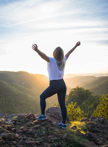 Person standing on a mountain top, arms raised, embracing the AIP Journey towards wellness and healing.