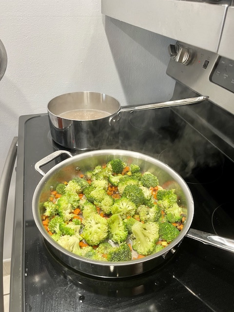 Carrots, celery, and broccoli florets cooking in a skillet on the stove, a step in preparing AIP-friendly Garlic Shrimp Cassava Orzo