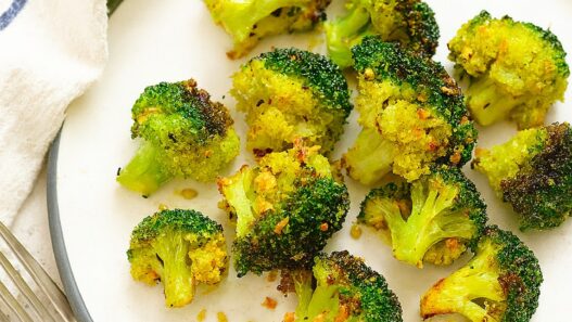 Garlic, turmeric roasted broccoli on a white plate with fork and napkin, healthy anti-inflammatory AIP side dish rich in fiber and antioxidants