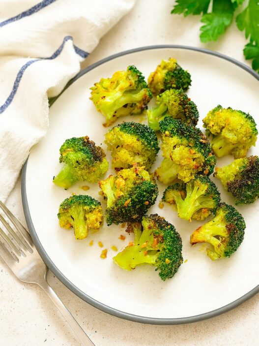Garlic, turmeric roasted broccoli on a white plate with fork and napkin, healthy anti-inflammatory AIP side dish rich in fiber and antioxidants