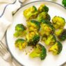 Garlic, turmeric roasted broccoli on a white plate with fork and napkin, healthy anti-inflammatory AIP side dish rich in fiber and antioxidants