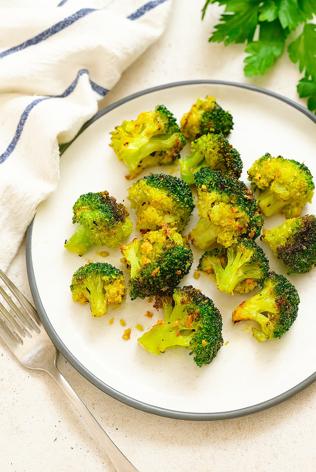 Garlic, turmeric roasted broccoli on a white plate with fork and napkin, healthy anti-inflammatory AIP side dish rich in fiber and antioxidants