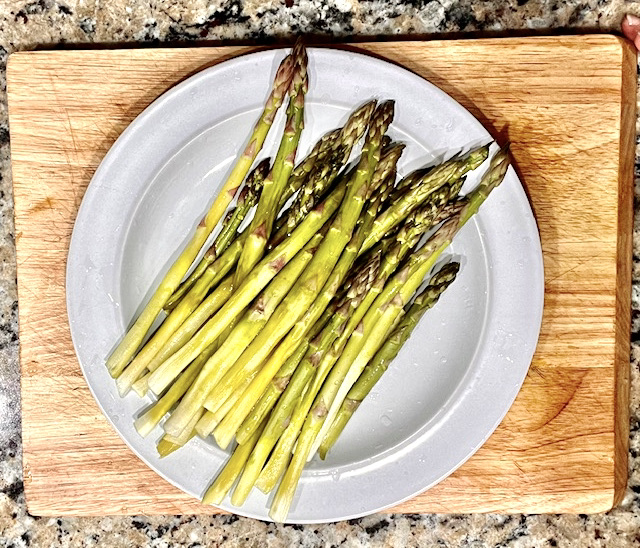 Fresh, cleaned, and trimmed asparagus spears on a plate, ready to be roasted or prepared for a healthy, AIP-friendly, and paleo dish.