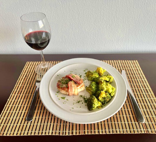 Bacon-wrapped pork chops with roasted garlic turmeric broccoli served on a plate.