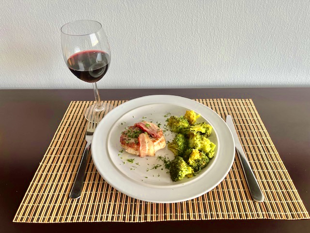 Bacon-wrapped pork chops with roasted garlic turmeric broccoli served on a plate.