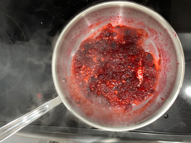 Preparing homemade cranberry sauce by simmering cranberries with maple syrup and lemon juice, ready to top AIP-friendly sweet potato cups for a delicious, gluten-free appetizer.