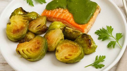 Roasted Brussels sprouts with ACV and maple syrup served with salmon and green herb sauce on a white plate, healthy AIP dinner, anti-inflammatory meal.