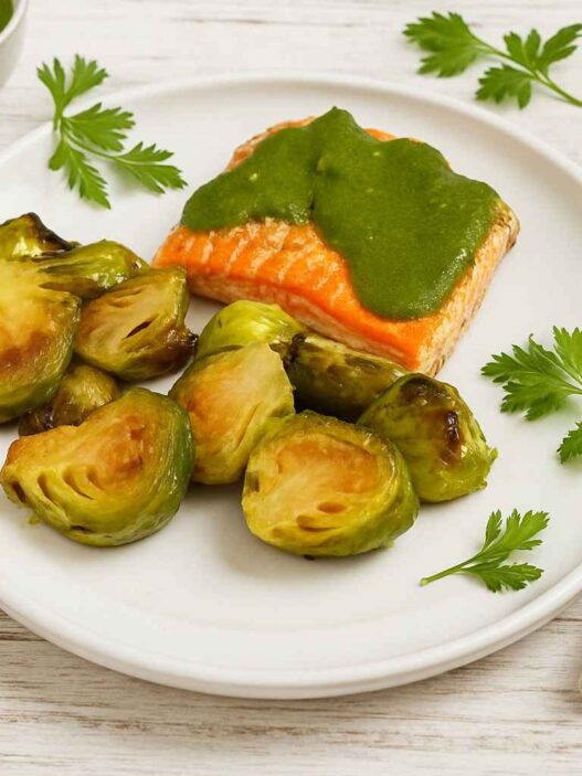 Roasted Brussels sprouts with ACV and maple syrup served with salmon and green herb sauce on a white plate, healthy AIP dinner, anti-inflammatory meal.