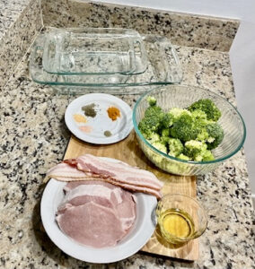 Ingredients for bacon-wrapped pork chops and roasted garlic turmeric broccoli, including pork chops, bacon, broccoli, turmeric, garlic, and avocado oil.