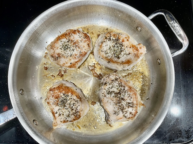 Pork chops searing in a pot on the stove, ready to be wrapped in bacon for a delicious meal.