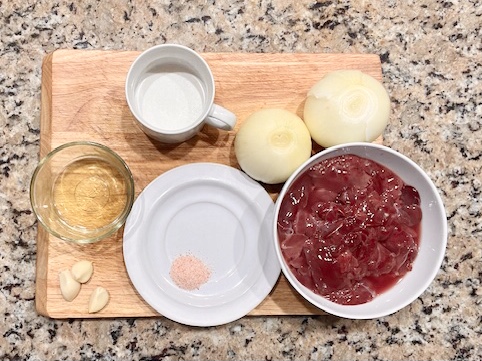 Ingredients for AIP Chicken Liver Pâté including chicken livers, onions, coconut milk, and thyme on a wooden board.