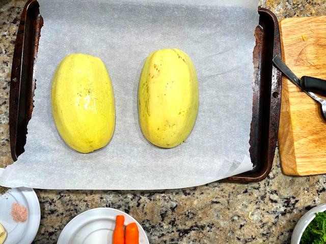 Halved spaghetti squash placed cut-side down on a baking sheet, ready to be roasted for a nourishing, gluten-free Spaghetti Squash Bowl.