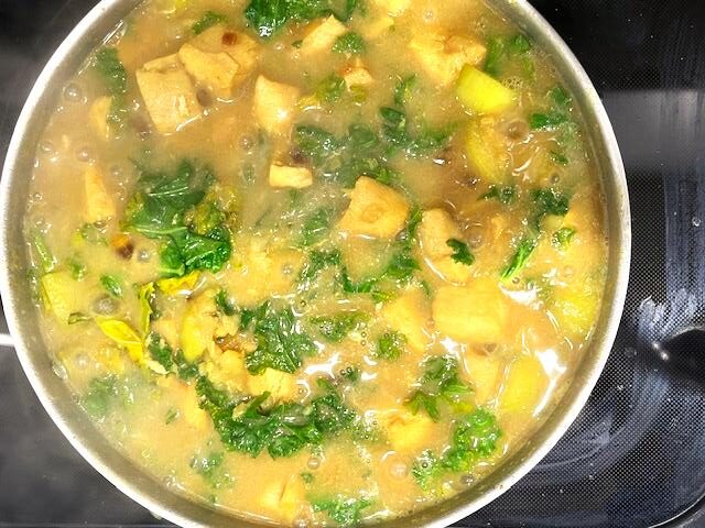 Cardamom-Infused Mahi-Mahi Curry cooking in a pan with coconut milk, sweet potato, zucchini, carrot, kale, and spices.