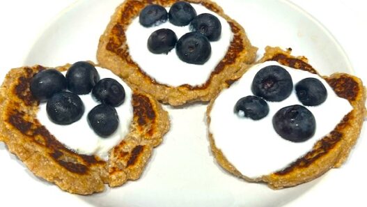 Three Delicious AIP Banana Pancakes topped with coconut yogurt and fresh blueberries on a white plate. A perfect gluten-free, dairy-free, and healthy breakfast!