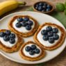 Delicious AIP Banana Pancakes topped with coconut yogurt and blueberries on a white plate, served on a rustic wooden table with a green towel – gluten-free, dairy-free, autoimmune-friendly.