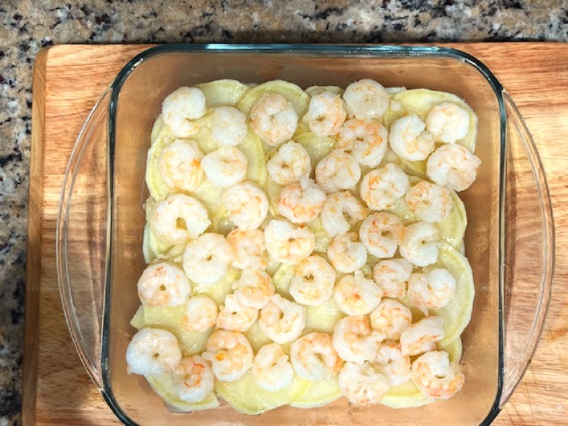 Cooked shrimp placed on top of parboiled sweet potato layers in a glass dish, prepared for an AIP Reintroduction Garlic Shrimp and Sweet Potato Gratin, a gluten-free, nightshade-free recipe.