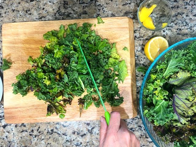 Chopping fresh kale on a wooden cutting board for Kale Sautéed with Cumin and Ghee.