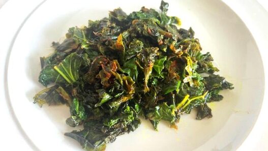 Kale Sautéed with Cumin and Ghee served on a white plate, garnished with lemon juice.