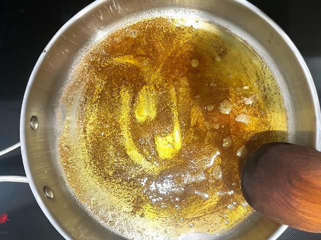 A pot on the stove with melted ghee, cumin, cinnamon, and turmeric for Kale Sautéed with Cumin and Ghee.