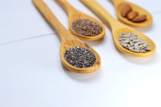 Nuts and seeds arranged on wooden spoons, including almonds, pumpkin seeds, and sunflower seeds.