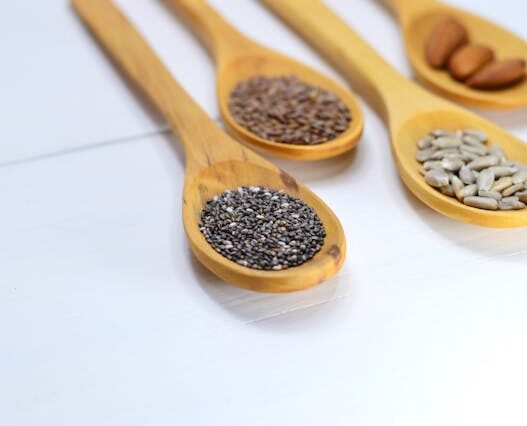 Nuts and seeds arranged on wooden spoons, including almonds, pumpkin seeds, and sunflower seeds.