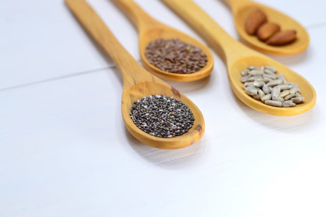 Nuts and seeds arranged on wooden spoons, including almonds, pumpkin seeds, and sunflower seeds.