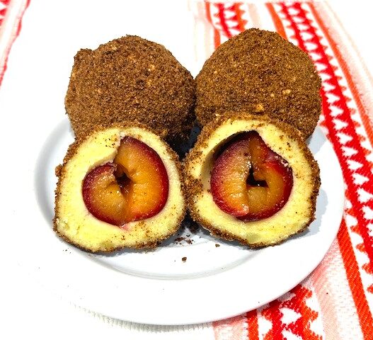 Two whole plums and one halved plum on a plate, showcasing their juicy texture—perfect for AIP-Friendly Plum Dumplings. This image highlights ingredients for a gluten-free, dairy-free, nut-free, nightshade-free dessert, ideal for the Autoimmune Diet and egg reintroduction.