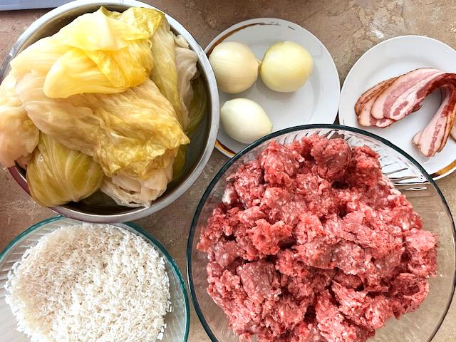 Ingredients for Romanian Cabbage Rolls (Sarmale) including ground pork, sauerkraut, rice, onions, thyme, and smoked bacon.