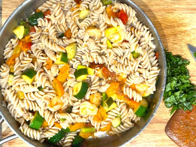 All ingredients for Shrimp and Veggie Pasta cooking in a skillet, including shrimp, zucchini, asparagus, cherry tomatoes, and gluten-free pasta.