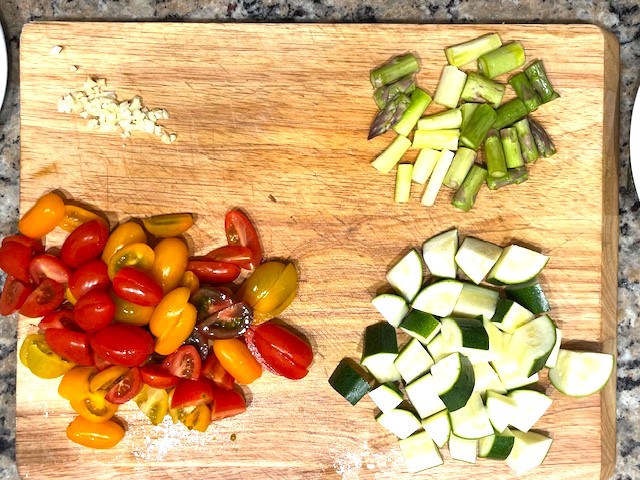 Chopping ingredients for Shrimp and Veggie Pasta, including zucchini, asparagus, and cherry tomatoes, for a gluten-free, dairy-free, AIP Reintroduction meal.