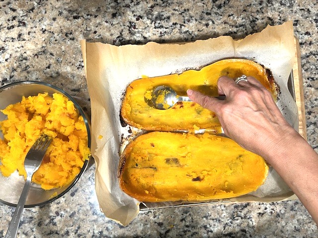 Roasted butternut squash with flesh being scooped, prepared for Savory Stuffed Butternut Squash. AIP reintroduction, gluten-free, dairy-free recipe.