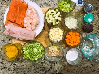 AIP Cioppino, a seafood stew ingredients arranged on a table, including fresh shrimp, salmon, mahi-mahi, onion, carrot, celery, garlic, coconut milk, and no-tomato sauce. Gluten free, tomato free and dairy free perfect for an Autoimmune, Anti-Inflammatory Diet
