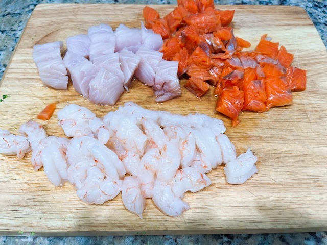AIP Cioppino, a seafood stew showing chopped shrimp, salmon, and mahi-mahi ready to be added to the pot for a flavorful, healthy seafood stew.