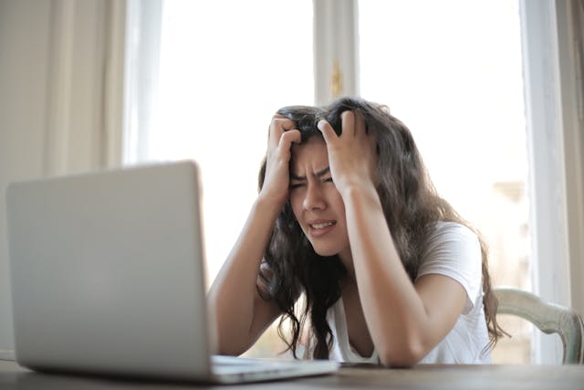 Woman experiencing headache and brain fog sitting at desk with laptop, illustrating Hashimoto’s thyroiditis and autoimmune brain health challenges, cognitive dysfunction, fatigue, and thyroid-related symptoms.
