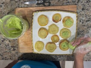 Hand piping avocado mixture into scooped sweet potato rounds to assemble Deviled No Eggs Potatoes.