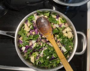 Rainbow Veggie Stew in progress with chopped bok choy purple cabbage mushrooms and leafy greens cooking in a stainless steel pan.