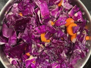 Chopped red cabbage and carrot slices simmering in a pot at the start of Sweet Potato Cabbage Stew.