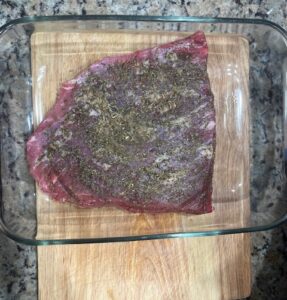 Best AIP Mouth-Melting Brisket rubbed with herbs and sea salt in a glass baking dish on a wooden board. Gluten free, dairy free, soy free, and nightshade free preparation for a tender slow-baked AIP brisket.