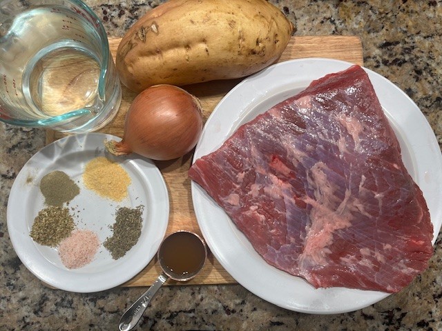 Best AIP Mouth-Melting Brisket ingredients displayed on a wooden board: raw brisket, white sweet potato, onion, apple cider vinegar, herbs, and filtered water. Gluten free, dairy free, soy free, nightshade free, and paleo friendly setup for autoimmune wellness.