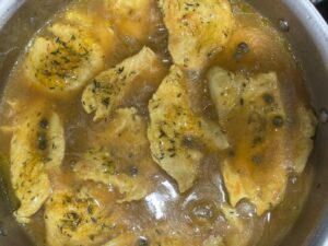 Healthiest AIP chicken piccata simmering in a stainless steel pan with lemon caper sauce and herbs for a gluten free and dairy free meal.