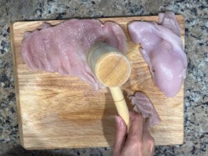 Healthiest AIP chicken piccata preparation showing chicken breast being tenderized on a wooden board with a meat mallet for an even, juicy result.